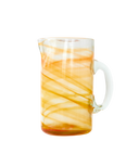 A clear glass pitcher with a white handle, decorated with diagonal bands of orange and yellow marbled swirls, isolated on a white background.