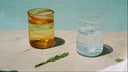 Two decorative drinking glasses on a concrete surface outdoors. The left glass is amber-tinted with a spiral pattern of orange, yellow, and green.