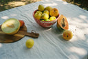 Fruits including a melon, apples, and a papaya on a white cloth outdoors.